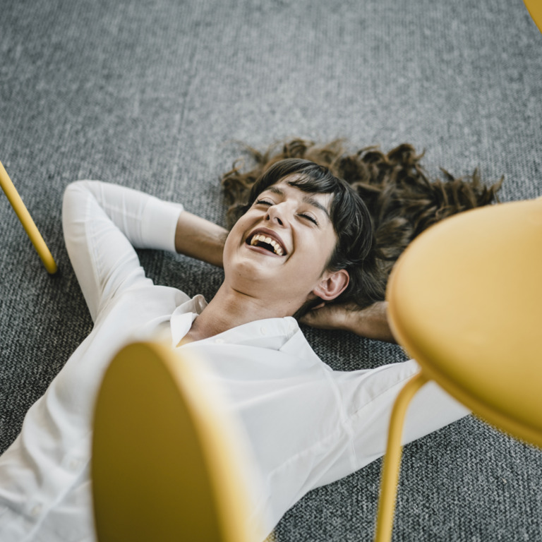 Frau liegt lachend auf Boden im Büro