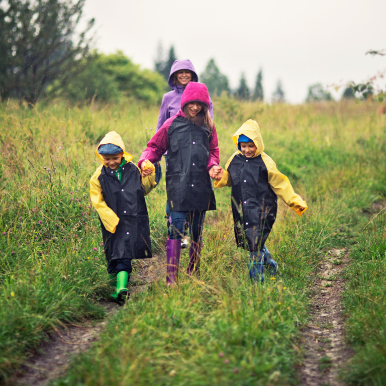 Junge Familie in Regenkleidung geht auf Feldweg spazieren.