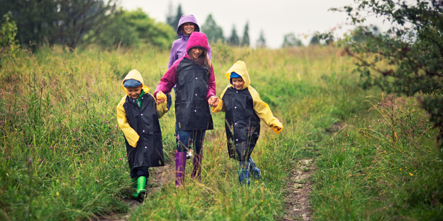 Kinder gehen lachend mit Regenmänteln auf einem Feldweg