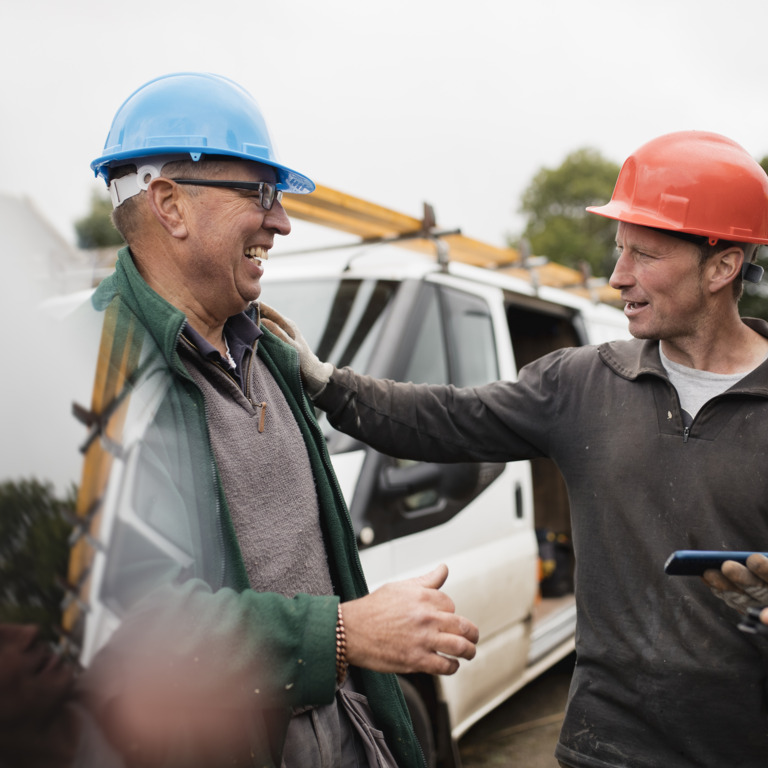 Zwei Männer mit Schutzhelmen unterhalten sich an einer Baustelle