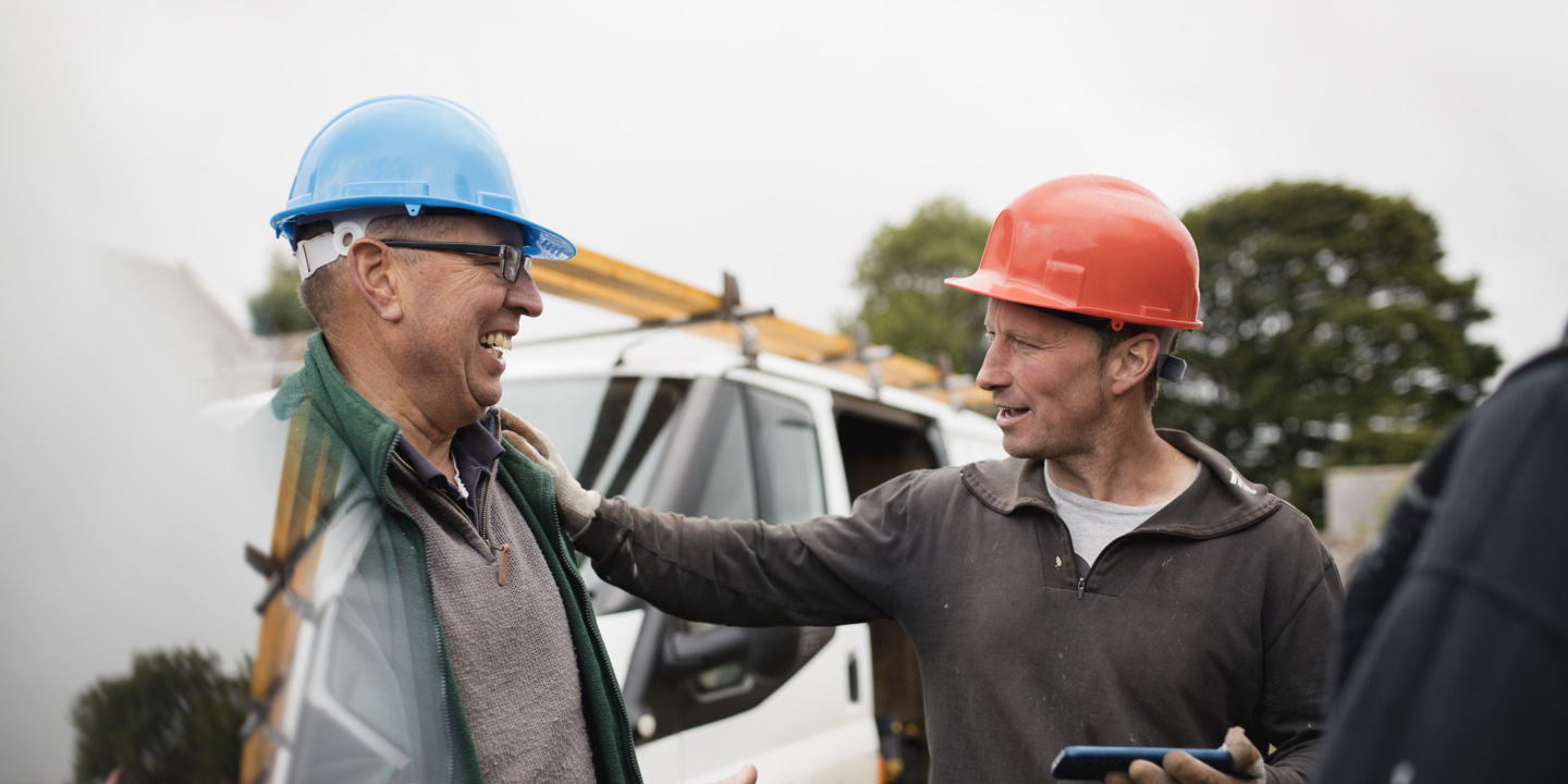 Zwei Handwerker stehen vor ihrem Lieferwagen und lachen miteinander