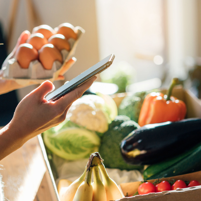 Frau mit Lebensmitteln und Smartphone in der Hand.