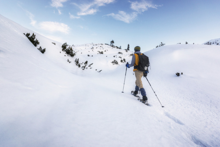 Mann auf Schneeschuhen wandert mit Skistöcken durch eine Schneelandschaft