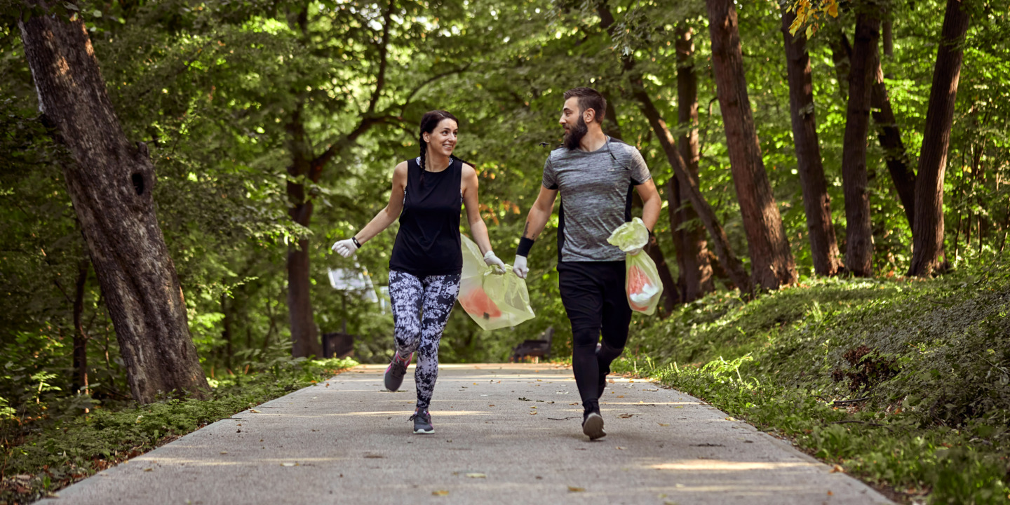 Mann und Frau joggen durch den Wald und sammeln Müll