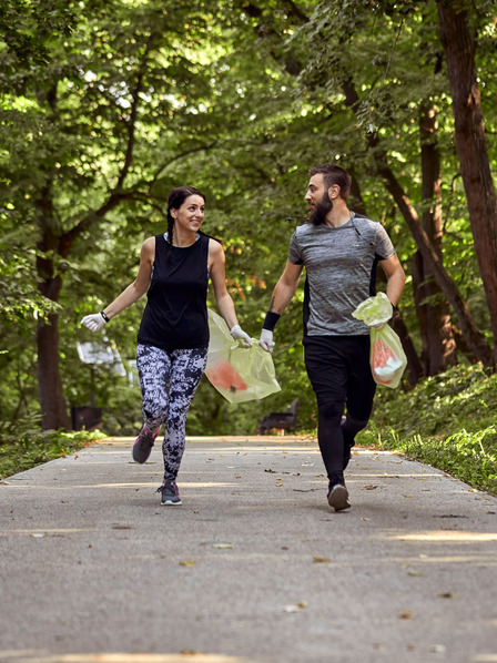 Mann und Frau joggen durch den Wald und sammeln Müll