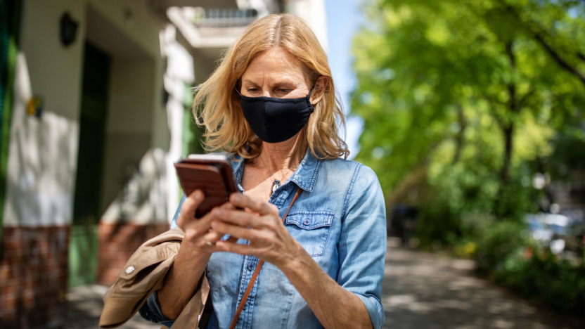 Frau mit Maske schaut im Freien auf ihr Handy.