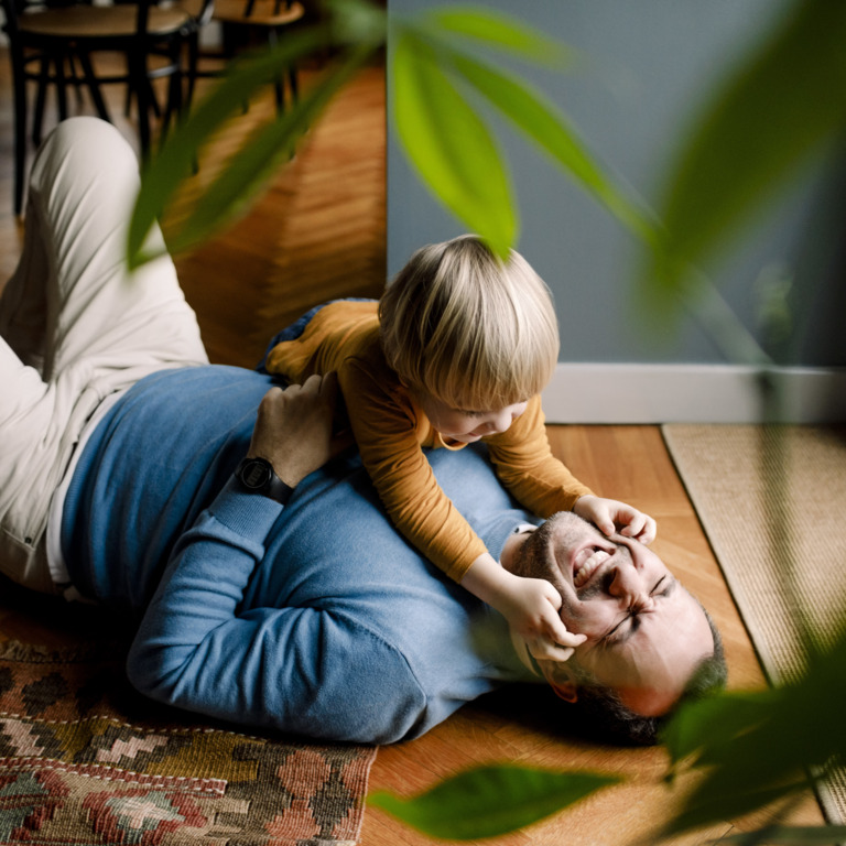 Vater und Kind toben am Boden auf dem Teppich