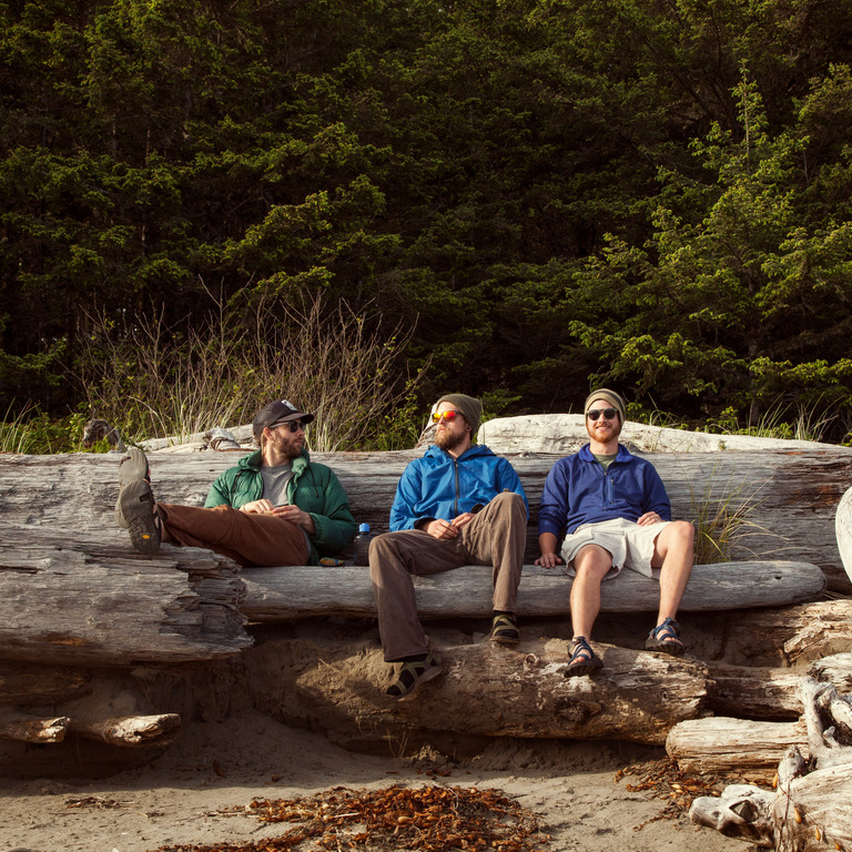 Drei Männer sitzen auf einem Baumstamm in der Natur