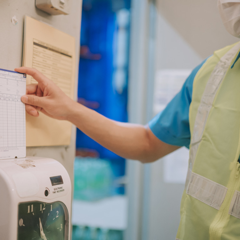 Person benutzt Stempelkarte in Stechuhr bei der Arbeit.