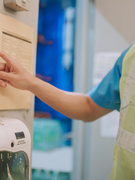 Person benutzt Stempelkarte in Stechuhr bei der Arbeit.