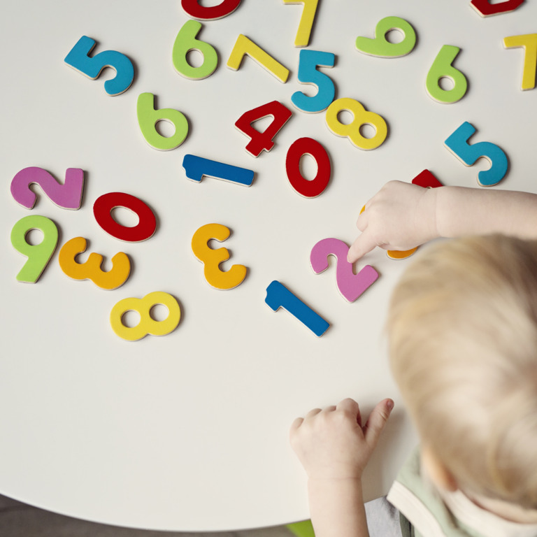 Kleinkind spielt mit Zahlen auf einem Tisch