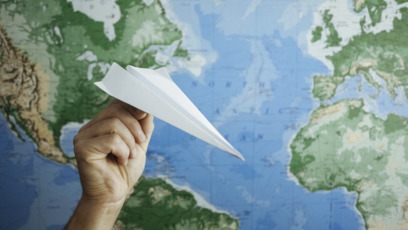 Hand hält Papierflieger vor Weltkarte