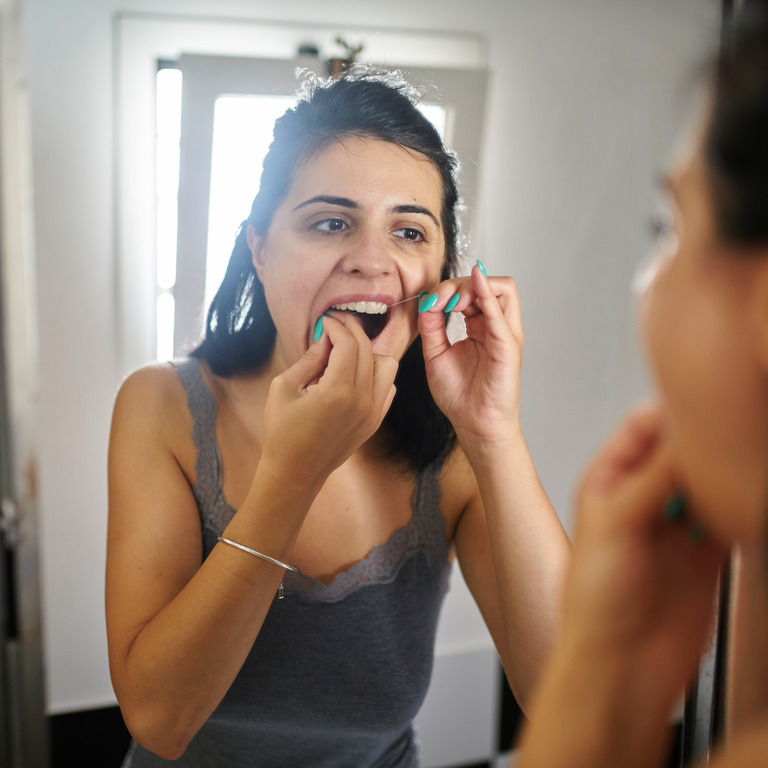 Mädchen reinigt mit Zahnseide am Spiegel ihre Zahnzwischenräume