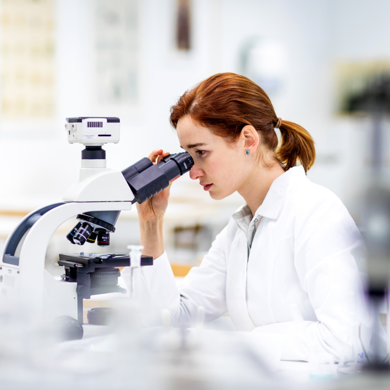 Junge Frau im Laborkittel schaut in ein Mikroskop