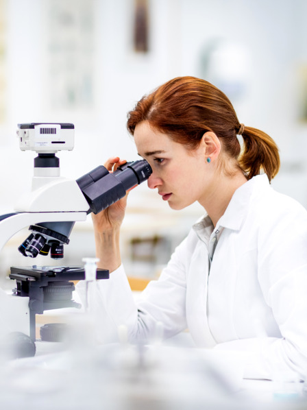 Auszubildende Laborassistentin im Kittel schaut durch ein Mikroskop