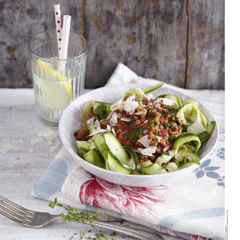 appetitlich in einem tiefen Teller angerichtete Portion Zoodles mit einem Glas selbstgemachter Zitronenlimonade